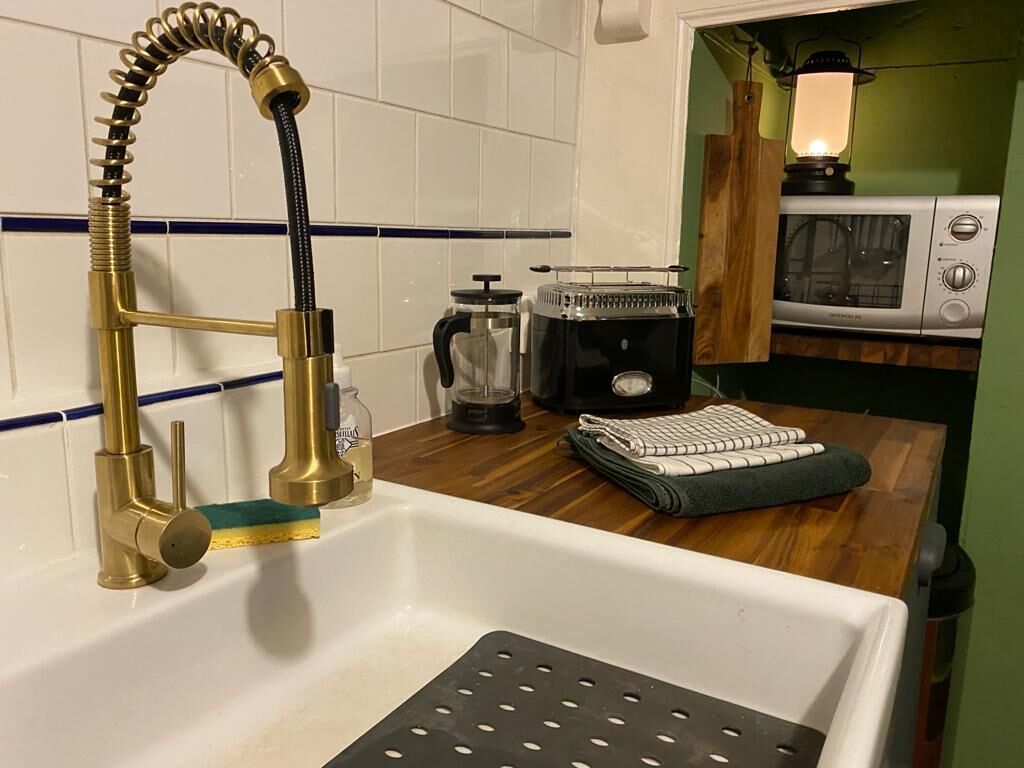 Une cuisine avec un évier blanc, un robinet doré, une machine à café et un four à micro-ondes.