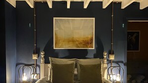A bedroom with a bed, two bedside lamps, a framed artwork on the wall, and a door with a rooster decoration.