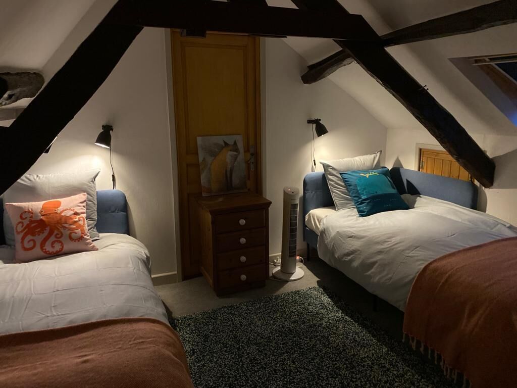 Ein gemütliches Schlafzimmer im Dachgeschoss mit zwei Betten, einer Holzkommode und einem Deckenventilator.