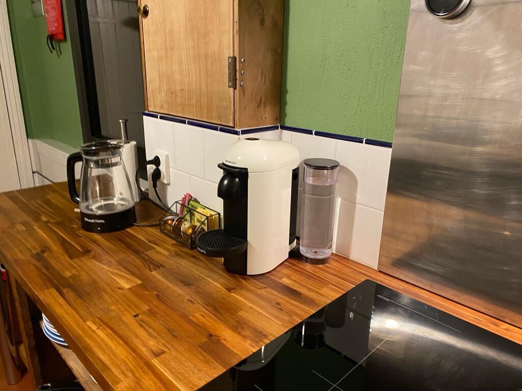 Una cocina con encimera de madera, cafetera, hervidor, licuadora y refrigerador de acero inoxidable.