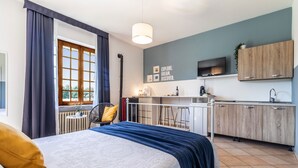 Ein modernes Hotelzimmer mit einem großen Bett, Blick ins Freie, einer Küchenzeile und einem Fernseher.