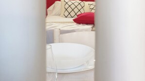 A white room with a bed, a red pillow, and a white chair. - Quick Home - Appartamento Narciso (Biella)