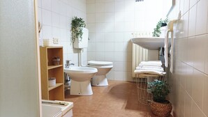 A bathroom with a toilet, bidet, sink, and shelves with toiletries. - Quick Home - Appartamento Narciso (Biella)