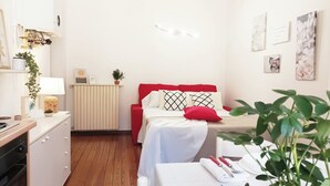 A neatly arranged bedroom with a red bed, white bedding, and a bedside table with a lamp and a plant. - Quick Home - Appartamento Narciso (Biella)
