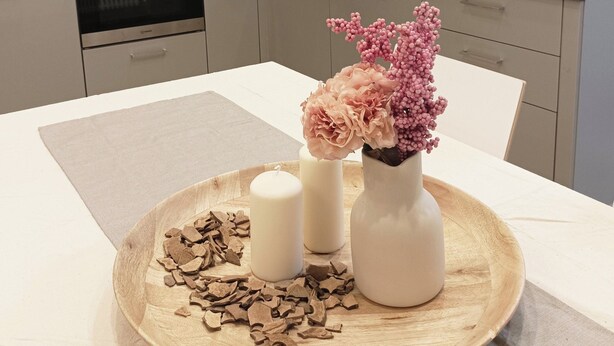 Une cuisine moderne équipée d’un four encastré, d’un évier et d’une fenêtre. On y trouve une table en bois sur laquelle est posée une assiette de chocolats et deux bougies.