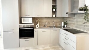 A modern kitchen with light-colored cabinets, a built-in oven, a microwave, a sink, and a stove. - Quick Home - Orchidea (Biella)