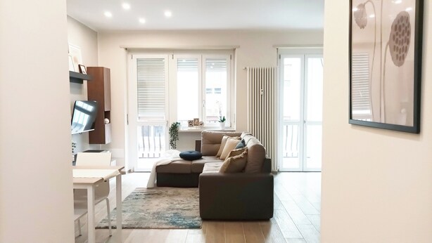 A modern living room with a sofa, a TV, and a dining area. - Quick Home - Orchidea (Biella)