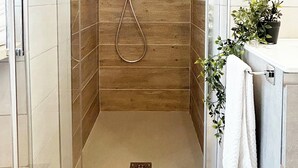 A walk-in shower with wooden paneling, a handheld showerhead, and a towel rack with a plant. - Quick Home - Orchidea (Biella)