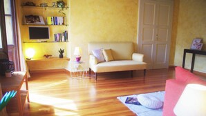 Un salon avec un canapé, un divan rouge, un téléviseur posé sur une étagère et une lampe.