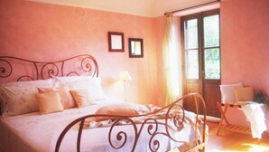 Une chambre à coucher avec un lit en métal, une table de chevet, une chaise et une fenêtre avec des rideaux.