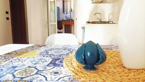 Una camera d'albergo con una coperta a motivi decorativi, un tappeto tessuto e vista sulla cucina e sul balcone attraverso una porta aperta.