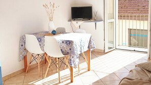 Una stanza con un tavolo da pranzo, sedie, una televisione e un balcone che si affaccia su un edificio.