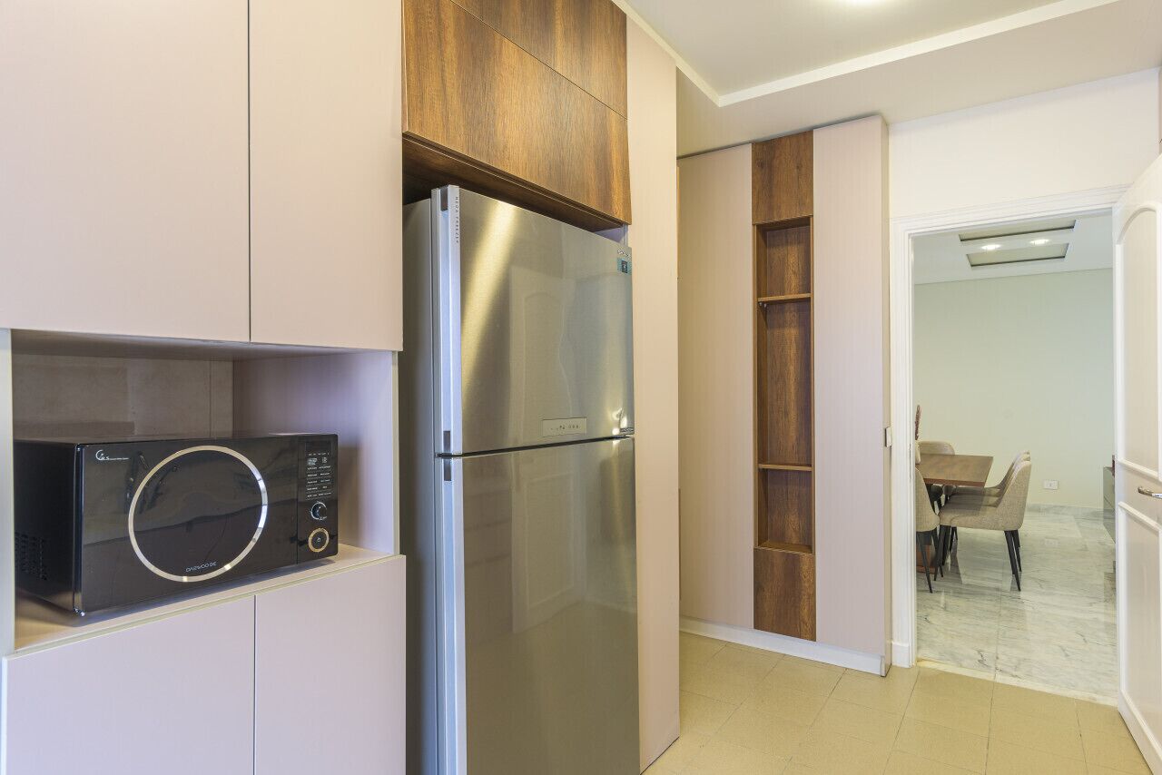 A compact kitchen with a stainless steel refrigerator, a microwave, and wooden cabinetry.