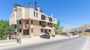 Un edificio de dos pisos con fachada de piedra, un coche estacionado adelante y un cielo azul despejado.