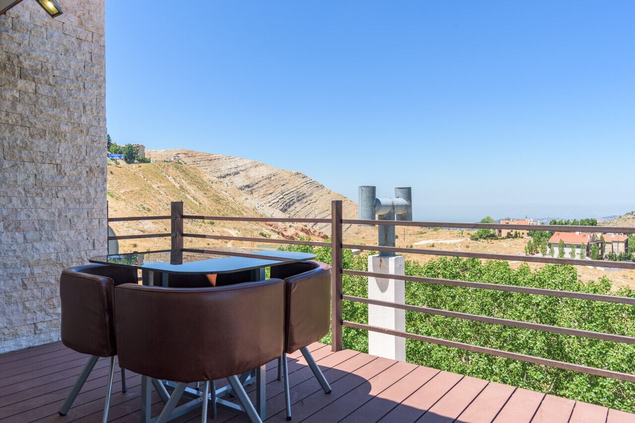 Un balcón con mesa y sillas, un muro de piedra y vistas a un paisaje montañoso.