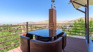 Un balcón con mesa y sillas, con vistas a un viñedo y colinas lejanas.