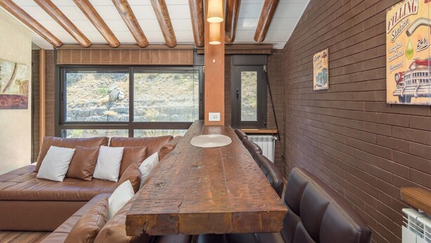 Comedor con una larga mesa de madera, asientos acolchados y vistas al exterior.
