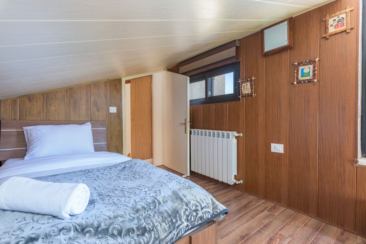 A bedroom with a bed, wooden walls, a window, and a radiator.