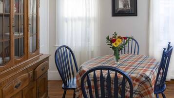Un comedor con mantel escocés, sillas azules, un armario de madera y un jarrón de flores.