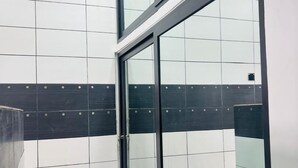 A modern bathroom with a glass shower enclosure, white tiled walls, and a dark horizontal stripe.