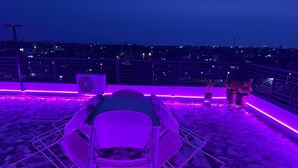 A rooftop terrace with a seating area and a view of the cityscape at night.