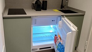 Eine kleine Küche mit integriertem Kühlschrank, einer Kaffeemaschine und einem Spülbecken.