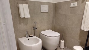 Ein Badezimmer mit einer Bidet-Funktion, Toilette, Waschbecken und einem Mülleimer.