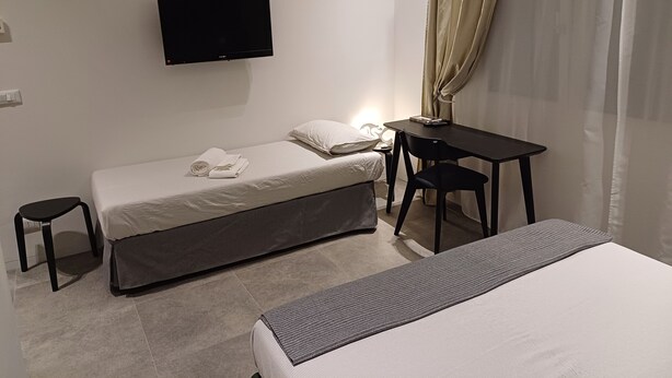 Ein modernes Hotelzimmer mit einem Einzelbett, einem Schreibtisch, einem Stuhl, einem an der Wand montierten Fernseher und einem kleinen Hocker.