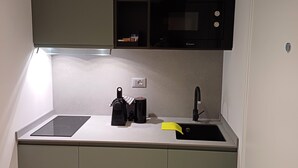 Eine kompakte Küche mit eingebauter Mikrowelle, einem kleinen Spülbecken und einer Arbeitsfläche mit Wasserkocher und Kaffeemaschine.