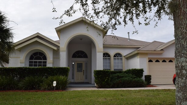 A two-story house with a front entrance under an arched window, a garage door, and a well-maintained lawn.