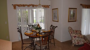 A dining area with a round table, chairs, and a hanging light fixture. There are two framed pictures on the wall and a window with blinds.