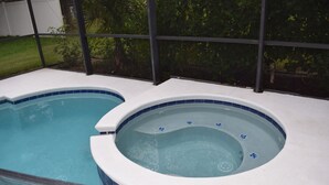 A swimming pool with a hot tub, surrounded by a covered area with a view of greenery.