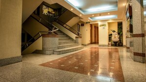 Eine Hotelhalle mit Treppe, einer Rezeption und einer Zierbrunnen.