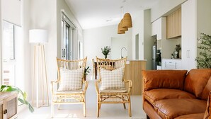 A modern living room with wicker chairs, a brown leather sofa, and a kitchen in the background.