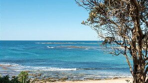 Una playa con agua azul cristalina, costa rocosa y un árbol en primer plano.