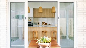 A modern kitchen with wooden cabinets, a dining area with a table and chairs, and a sliding glass door leading to a patio.