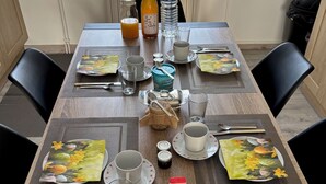 A dining table set with plates, cups, and cutlery, with a bottle of juice and a thermos on it. - A pleasant room with shower room, 160cm bed and all comforts included. (Lavelanet)