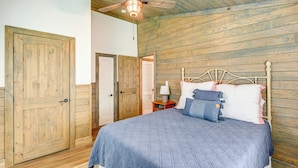 Un dormitorio con techo de madera, una cama con cabecera y una mesita de noche con lámpara.