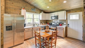 Una cocina con paredes de madera, un refrigerador de acero inoxidable, una mesa de comedor de madera con sillas y armarios blancos.