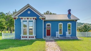 Una casa pequeña de un piso con fachada azul, una puerta roja y un camino de ladrillos que lleva a la entrada.