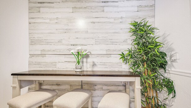 A dining area with a white table and three cushioned stools, a vase with white flowers, and a tall green plant in a basket. - Hollywood Hideaway: Close to Dtwn & Beaches (Hollywood)