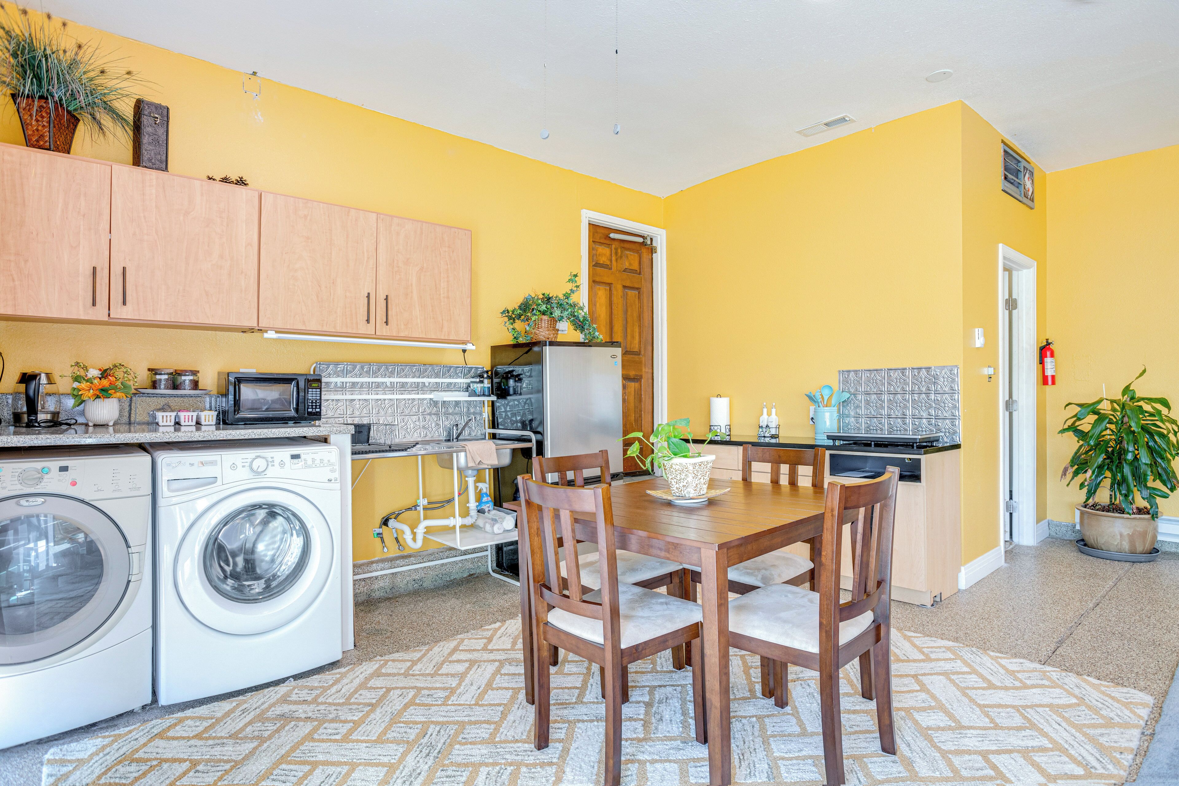 A compact kitchen with a dining area, washing machine, microwave, and a potted plant.