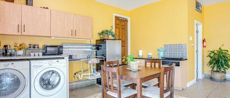 A compact kitchen with a dining area, washing machine, microwave, and a potted plant.