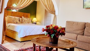 A bedroom with a bed, a nightstand, a lamp, a coffee table with a vase of flowers, and a sofa. - Riad salix agafay (Saada)