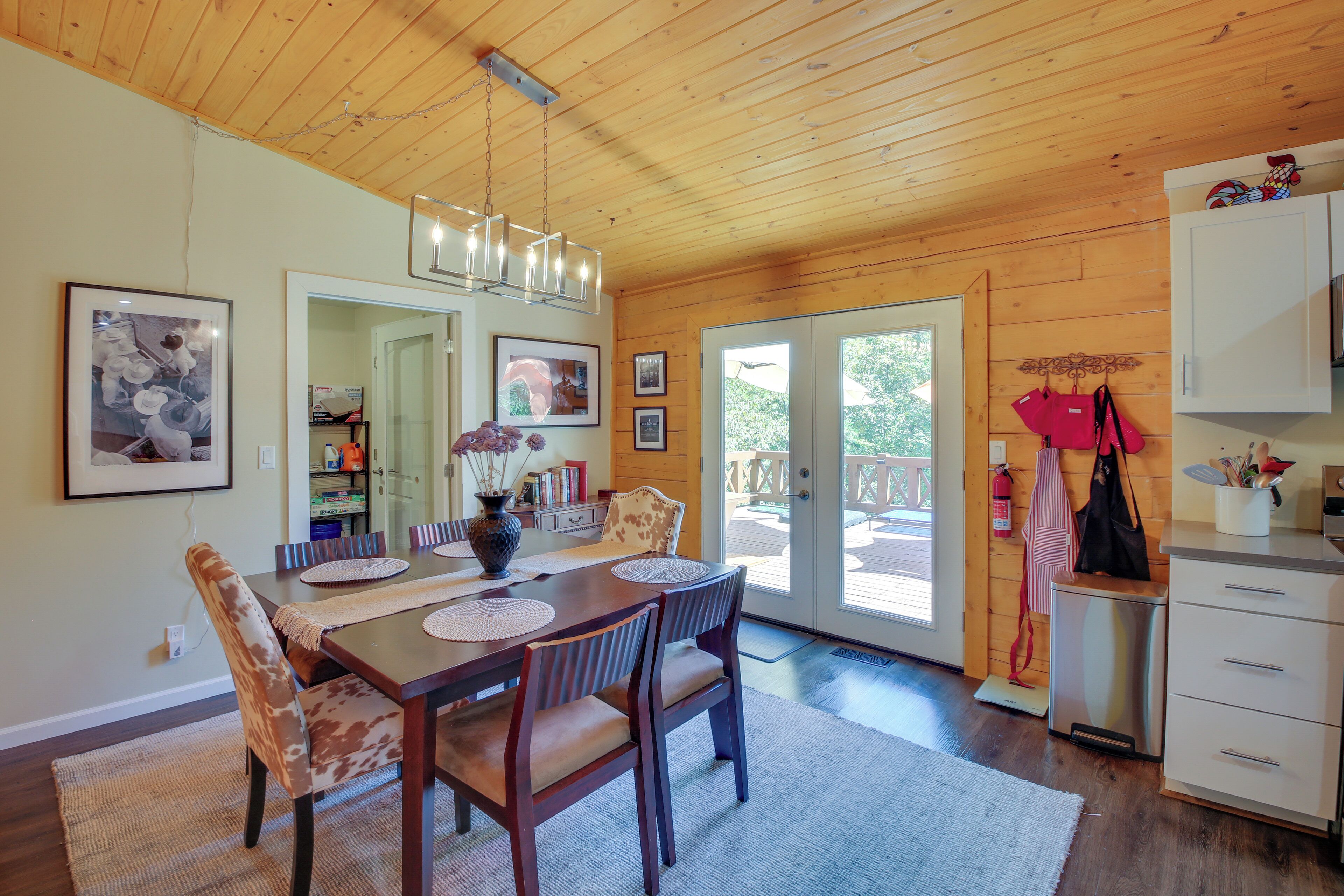 A wooden interior with a dining table, chairs, a chandelier, and a kitchen area with cabinets and a countertop.