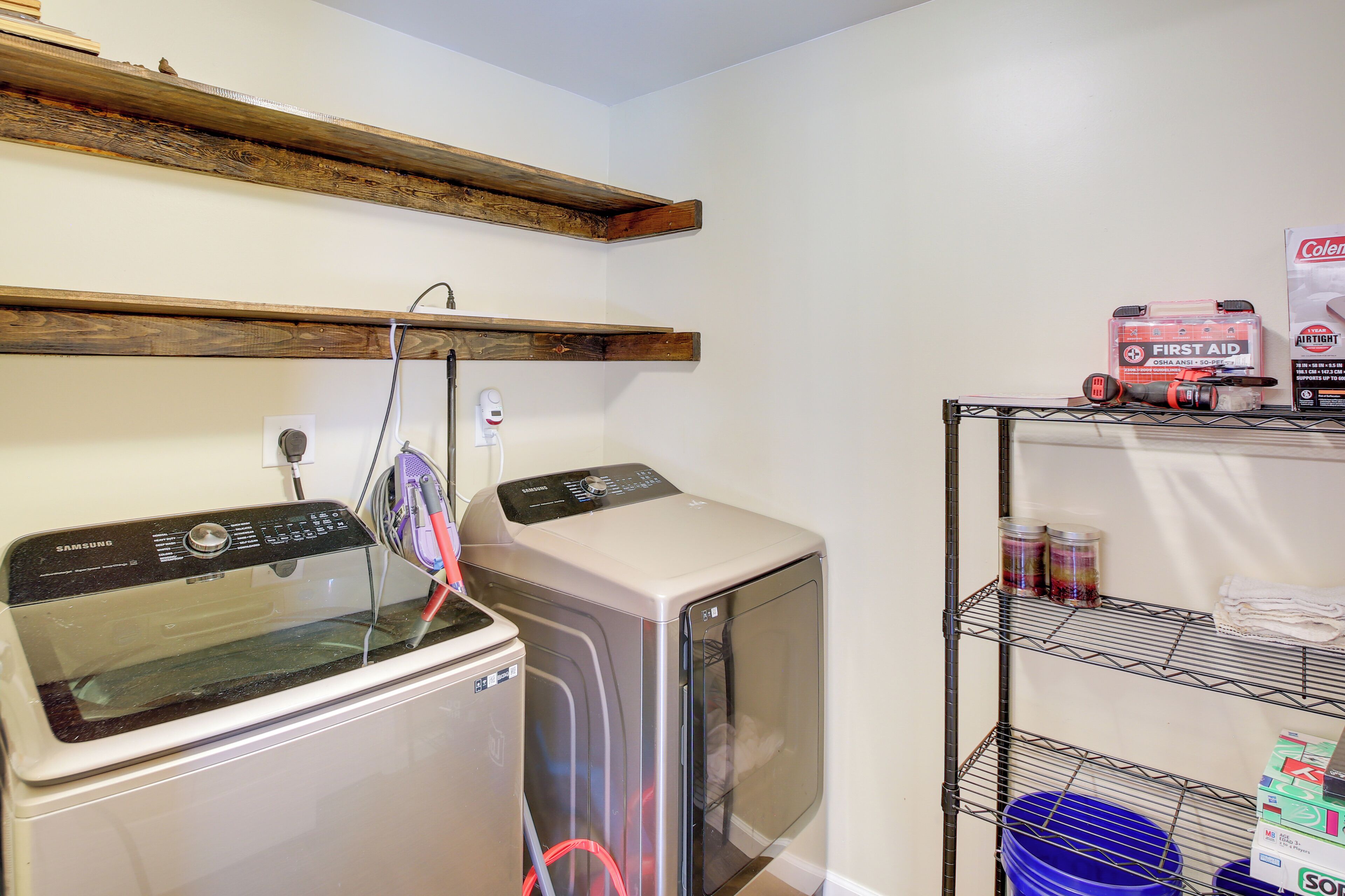 A laundry area with a washing machine and dryer, a shelf with cleaning supplies, and a wooden beam ceiling.