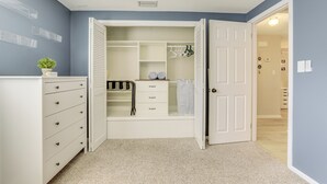 Un dressing sans porte, une commode blanche et une petite plante posée sur la commode.