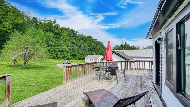 Une terrasse en bois, agréée de mobilier d’extérieur et d’un parasol rouge, qui offre une vue sur une pelouse et une colline boisée.