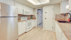 Una cucina moderna con mobili bianchi, frigorifero in acciaio inossidabile, forno a microonde e forno integrato.