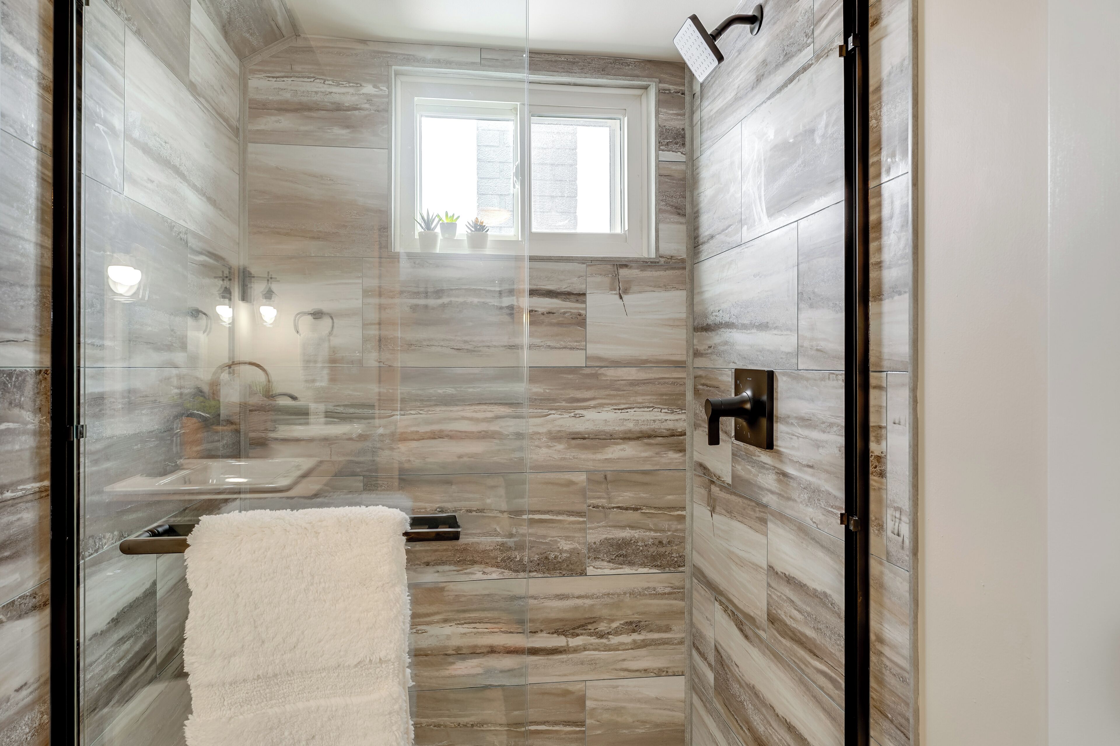 Une salle de bain moderne avec une douche à parois de verre, une fenêtre et une serviette blanche posée sur un porte-serviettes.